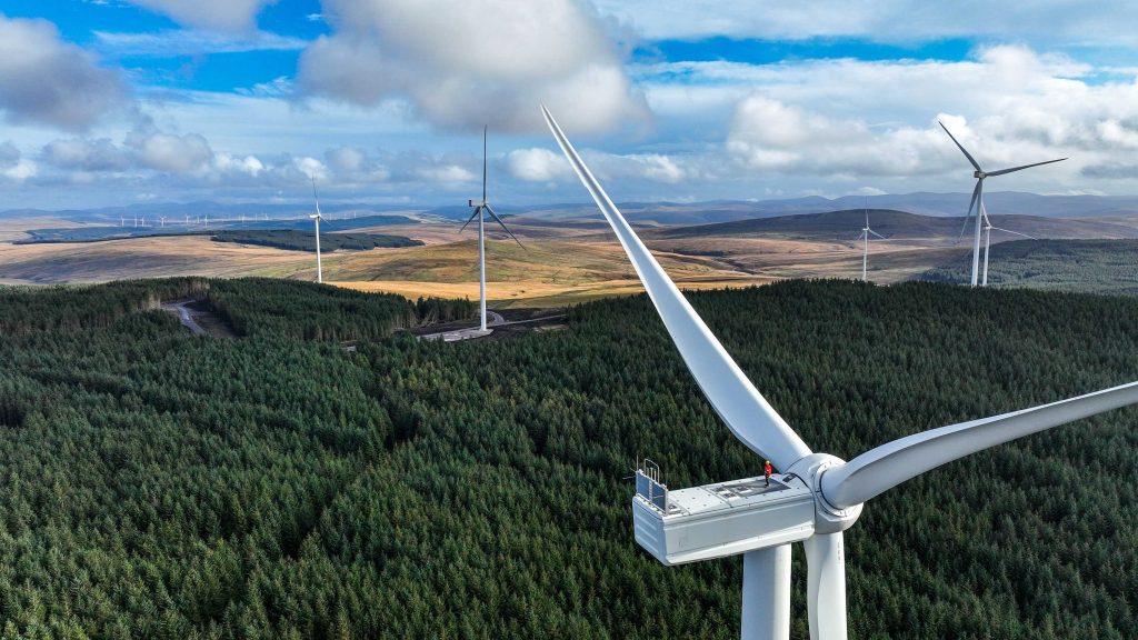 An employee of Perigus Energy is standing on a wind turbine in Scotland with multiple turbines in the background